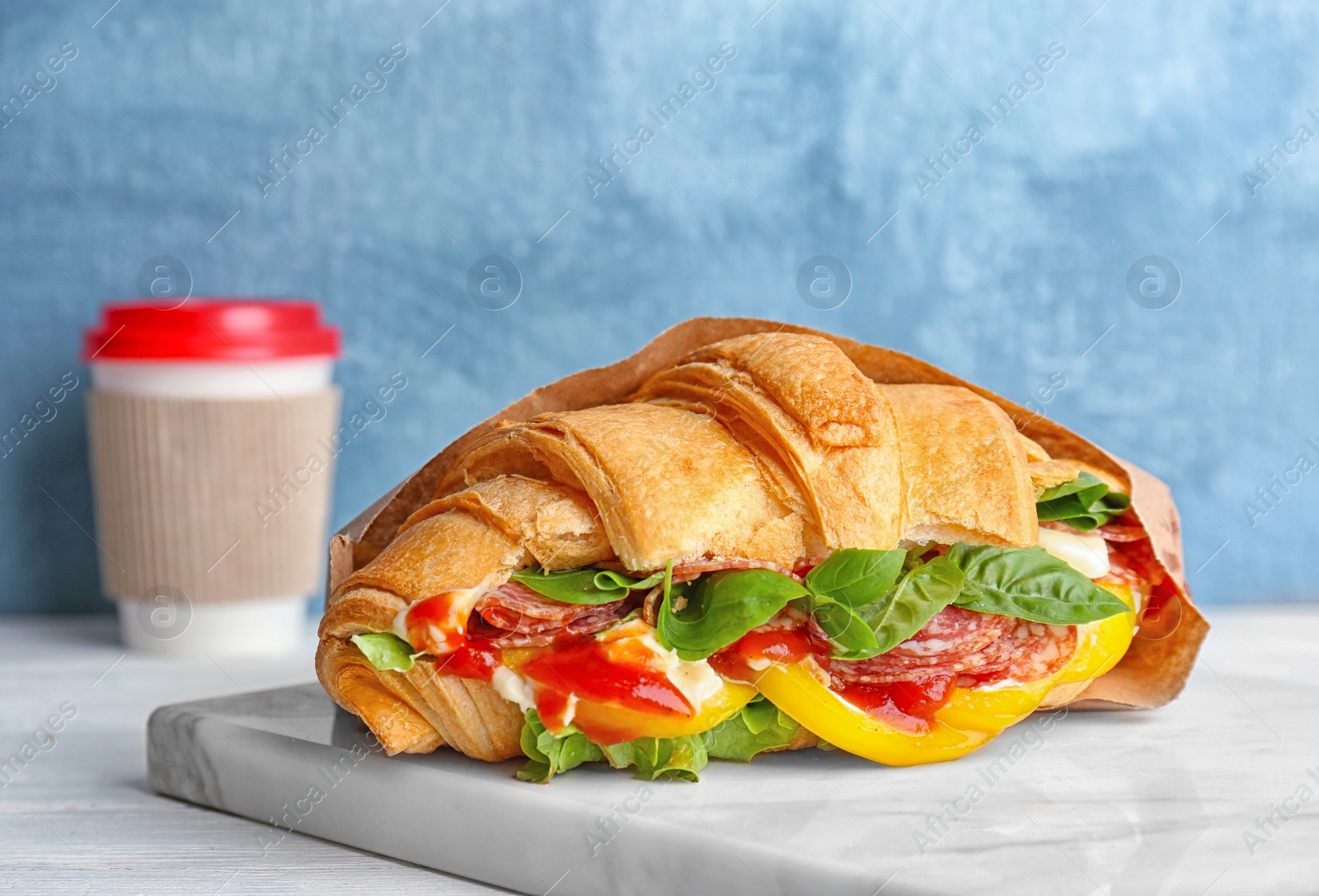 Photo of Tasty croissant sandwich with salami on table