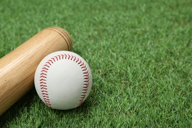 Photo of Wooden baseball bat and ball on green grass, closeup. Space for text