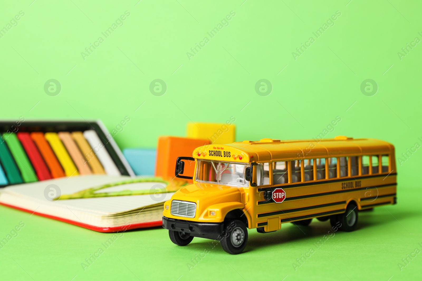 Photo of School bus model and stationery on green background. Transport for students