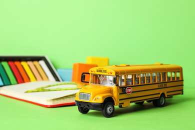 Photo of School bus model and stationery on green background. Transport for students