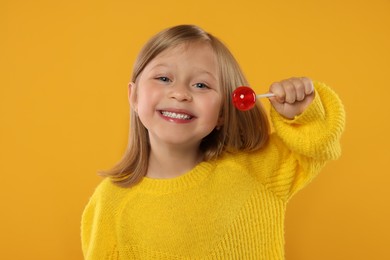 Happy girl with lollipop on orange background