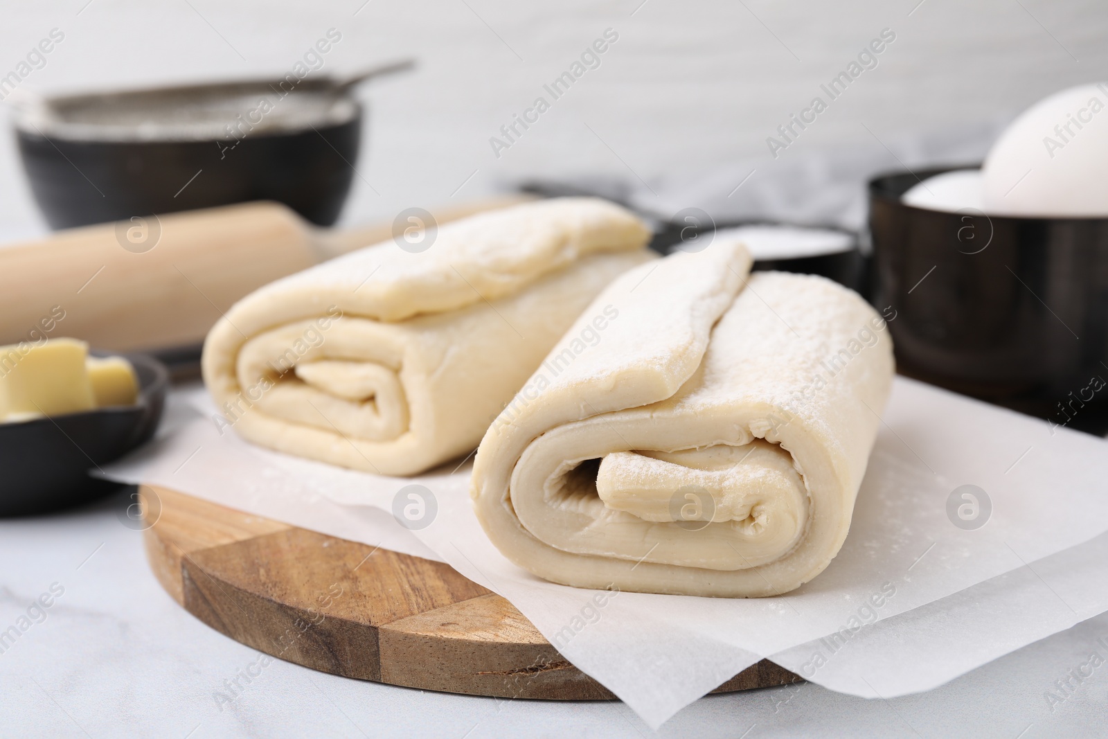 Photo of Raw puff pastry dough on white marble table, closeup