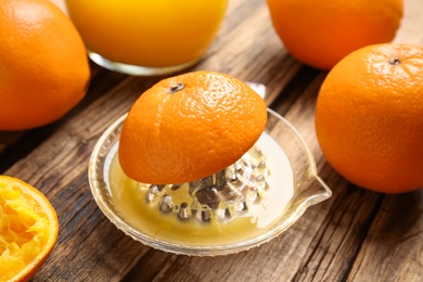 Photo of Fresh ripe oranges and squeezer on wooden table, closeup