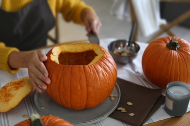 Photo of Woman carving pumpkin at table in kitchen. Halloween celebration