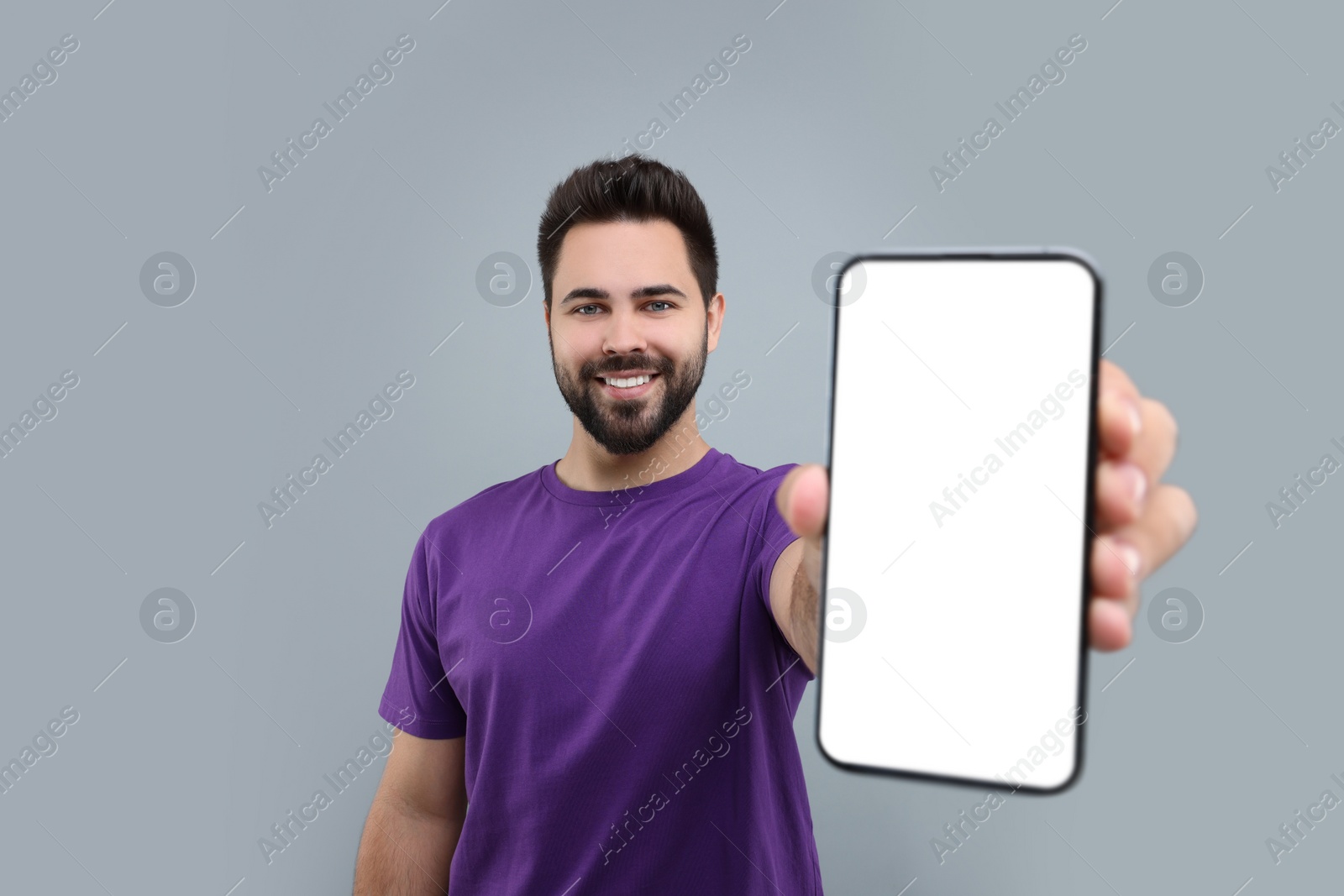 Photo of Young man showing smartphone in hand on light grey background