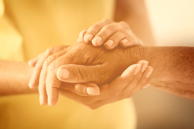 Volunteer and elderly woman holding hands in sunlit room, closeup