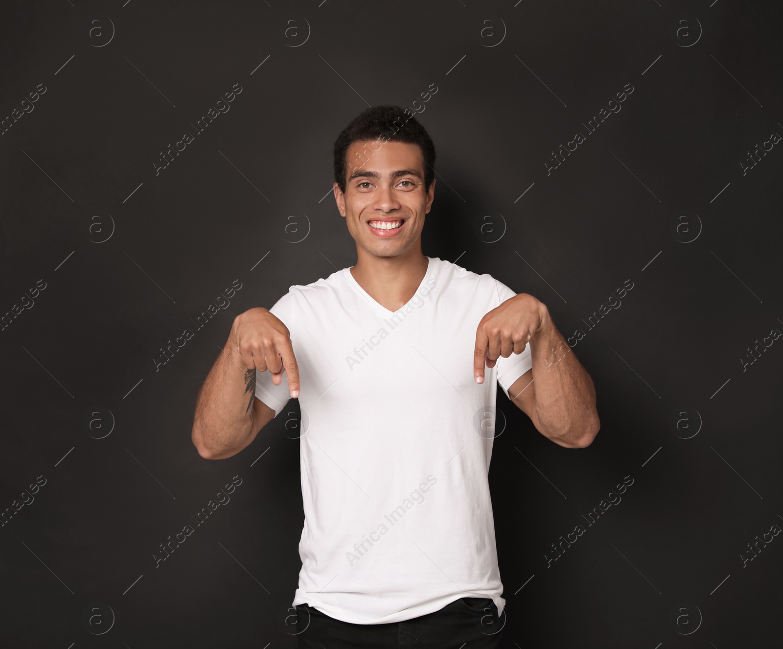 Photo of Handsome young African-American man pointing down on black background