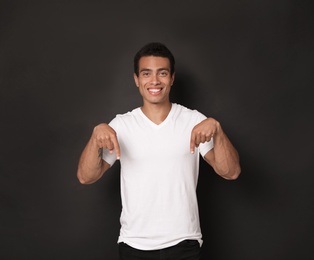 Photo of Handsome young African-American man pointing down on black background