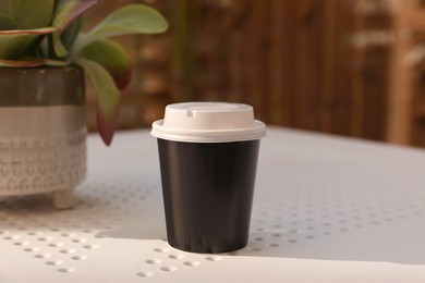 Photo of Takeaway paper cup with plastic lid on white table indoors