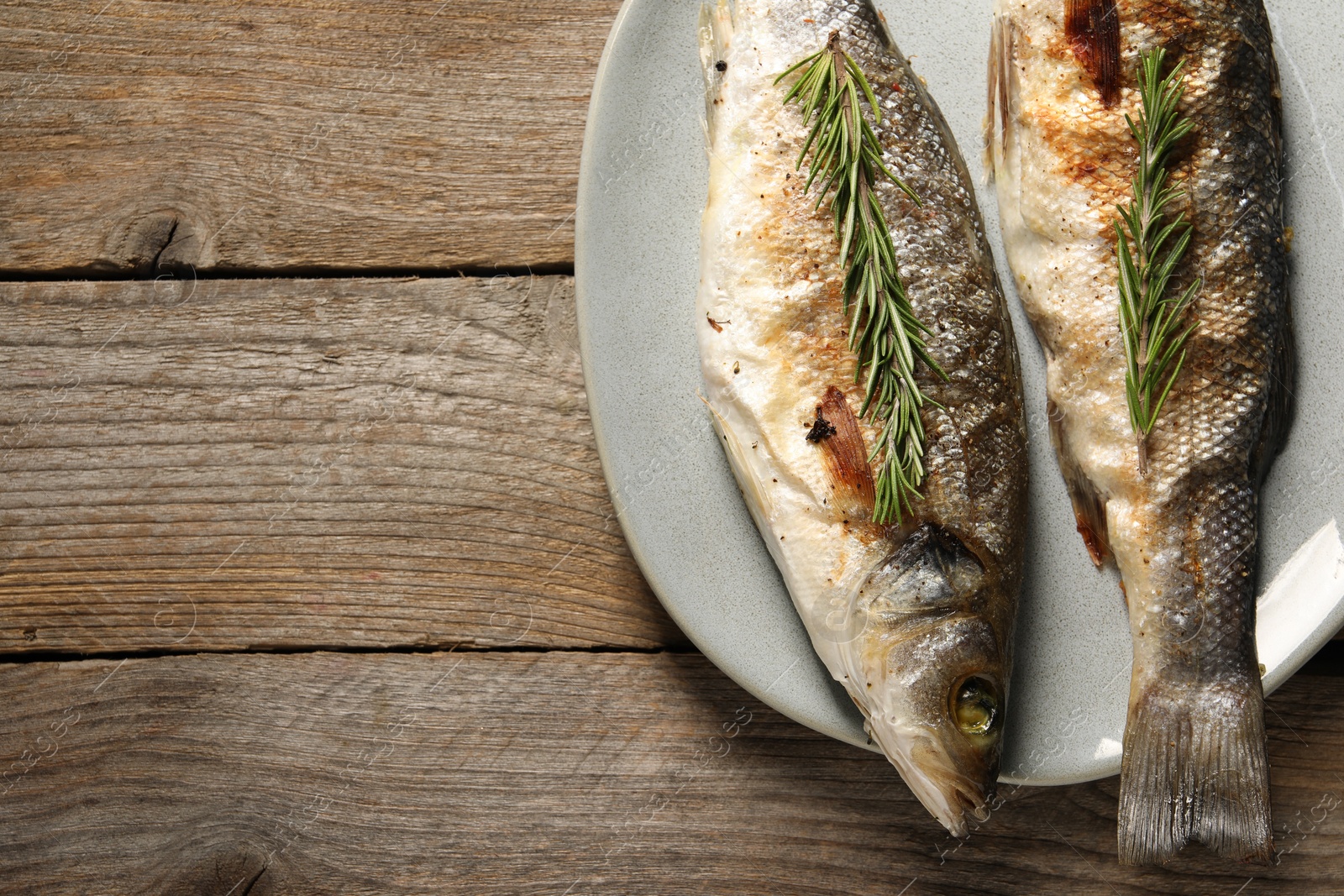 Photo of Delicious baked fish and rosemary on wooden table, top view. Space for text