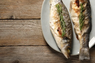 Photo of Delicious baked fish and rosemary on wooden table, top view. Space for text