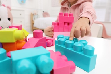 Cute little girl playing with colorful building blocks at table in room, closeup