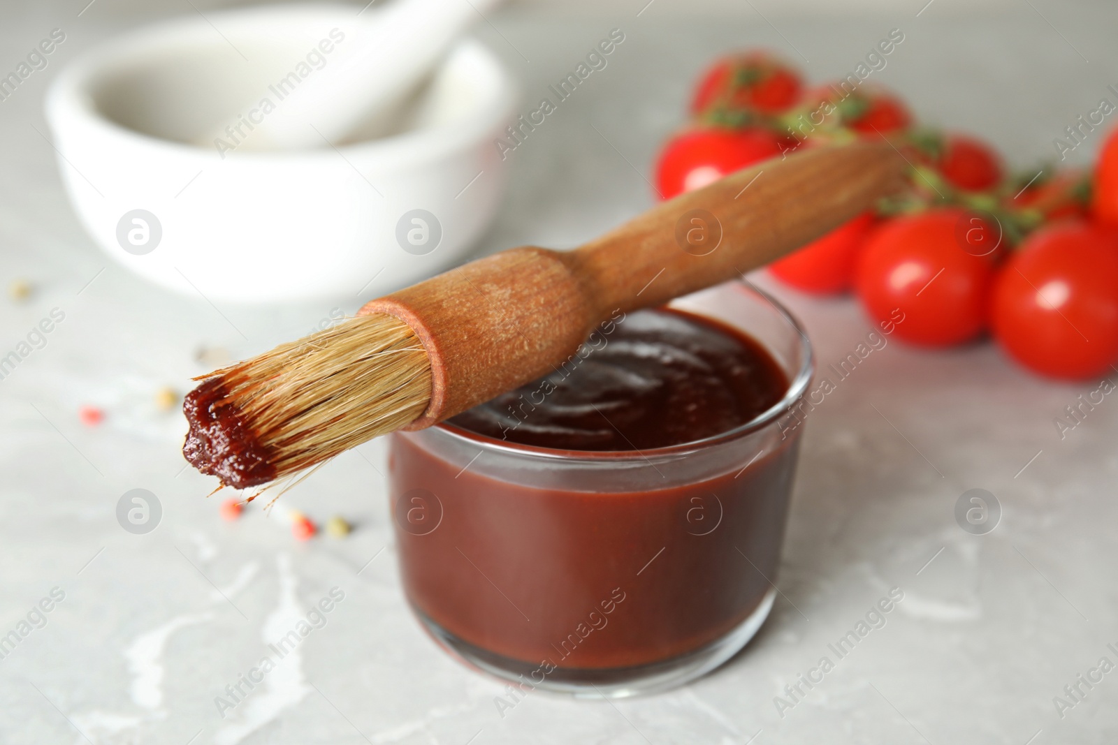 Photo of Glass bowl of barbecue sauce with basting brush on table