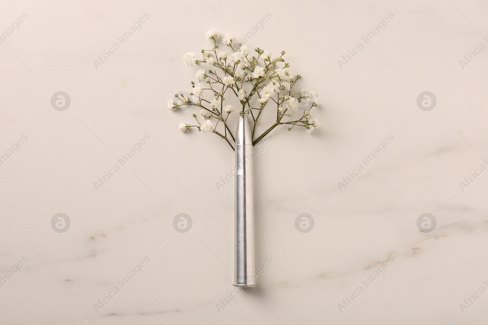 Photo of Metal bullet and beautiful gypsophila flowers on light marble table, flat lay
