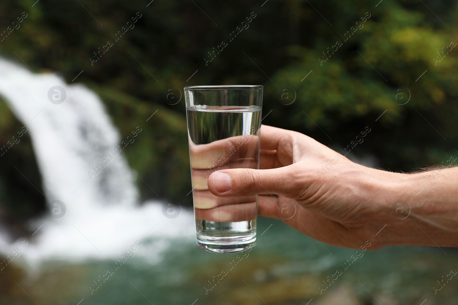 Photo of Man holding glass of fresh water near waterfall, closeup