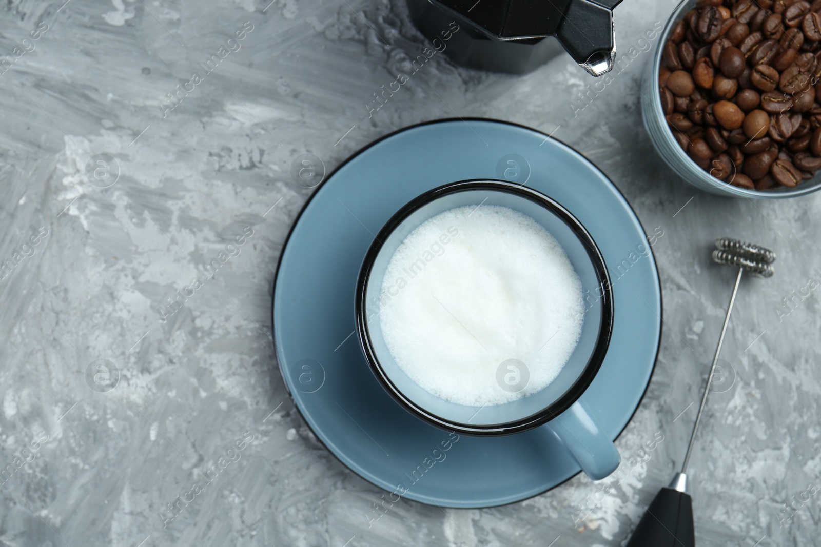 Photo of Mini mixer (milk frother), whipped milk in cup and coffee beans on grey textured table, flat lay. Space for text