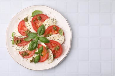 Plate of delicious Caprese salad with pesto sauce on white tiled table, top view. Space for text