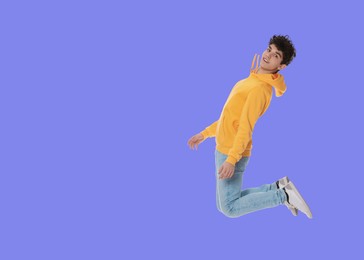 Teenage boy jumping on light blue background, space for text