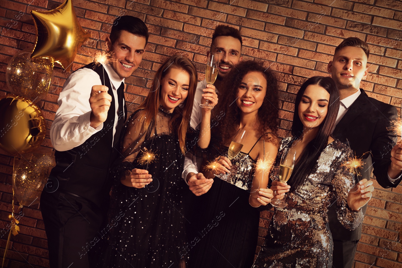 Photo of Happy friends with glasses of sparkling wine and sparklers celebrating New Year indoors