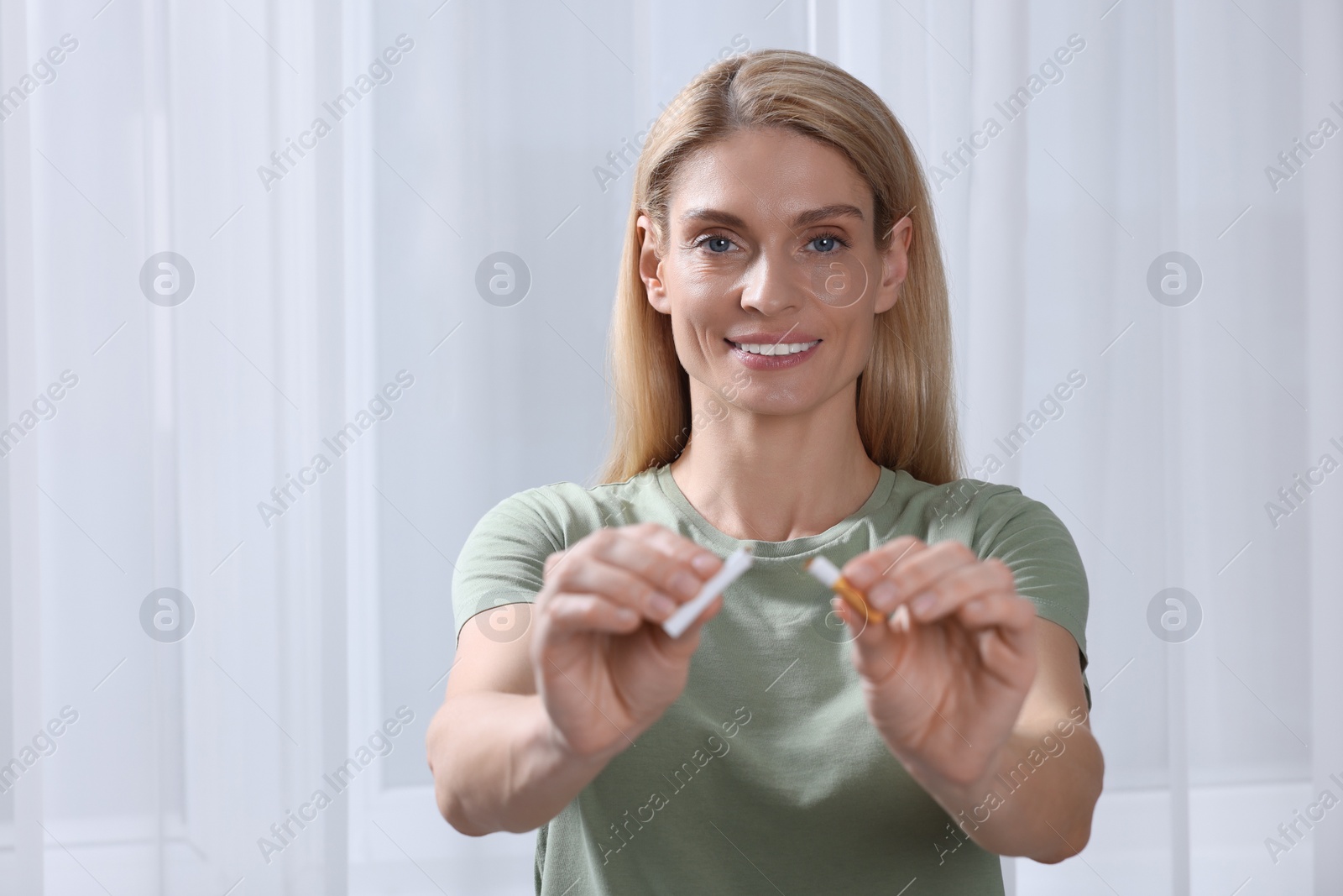 Photo of Happy woman with broken cigarette on light background. Quitting smoking concept