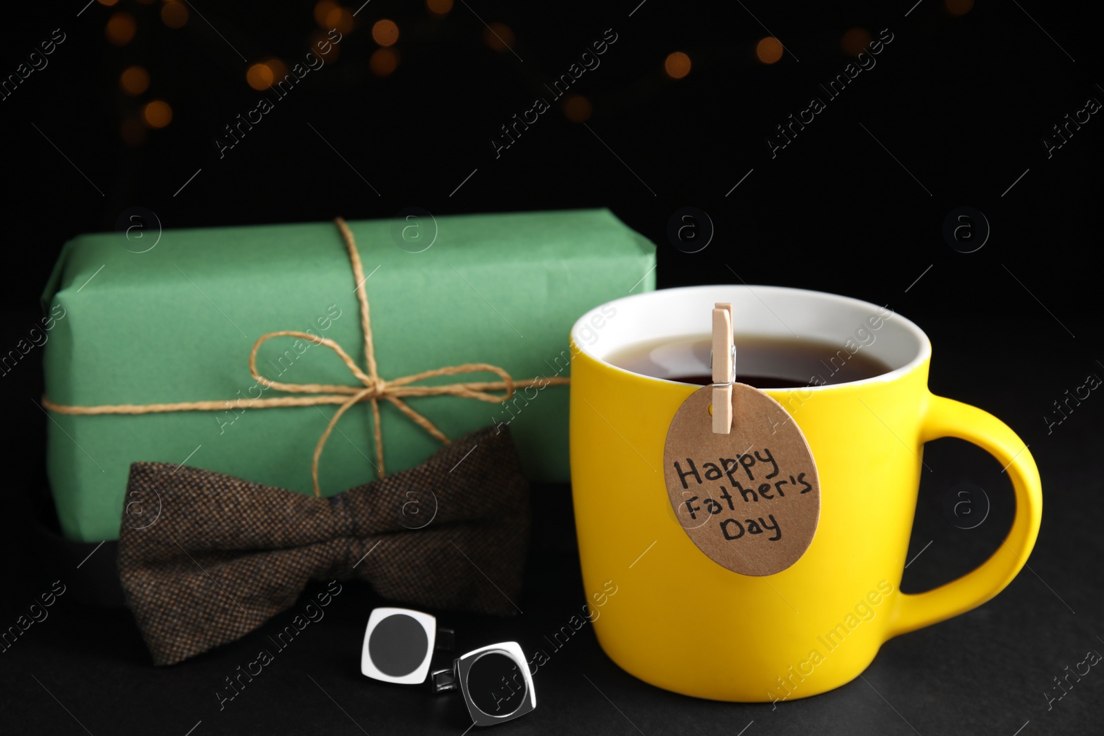 Photo of Composition with cup of tea and tag HAPPY FATHER'S DAY on black table against blurred background