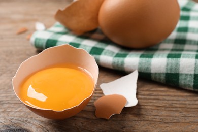 Photo of Cracked raw chicken egg with yolk on wooden table, closeup