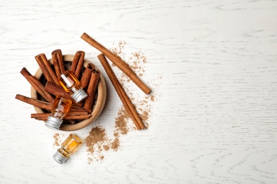 Bowl with bottles of cinnamon oil and sticks on wooden background