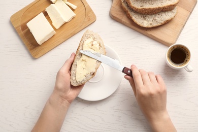 Photo of Woman spreading butter on slice of bread over table, closeup