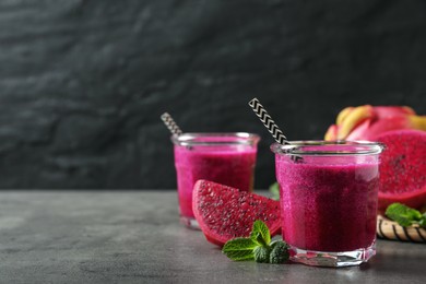 Photo of Delicious pitahaya smoothie, fruits and fresh mint on grey table, space for text
