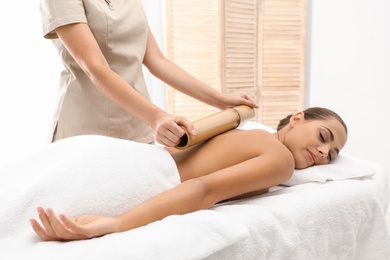 Photo of Young woman having massage with bamboo stick in wellness center