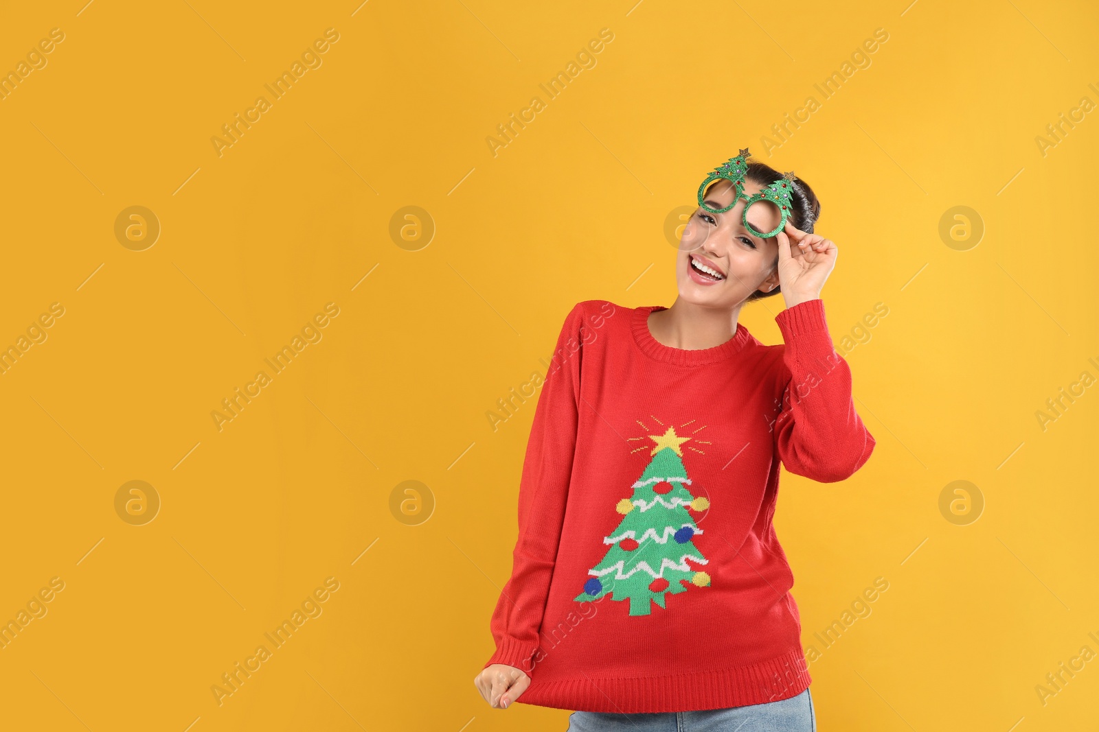 Photo of Young woman in Christmas sweater and party glasses on yellow background, space for text