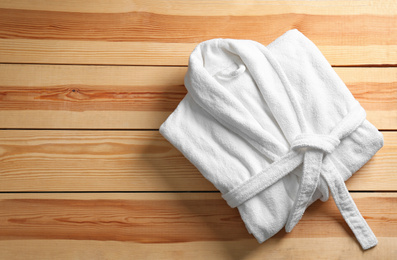 Photo of Clean folded bathrobe on wooden background, top view. Space for text