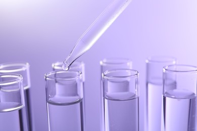 Dripping liquid from pipette into test tube on violet background, closeup