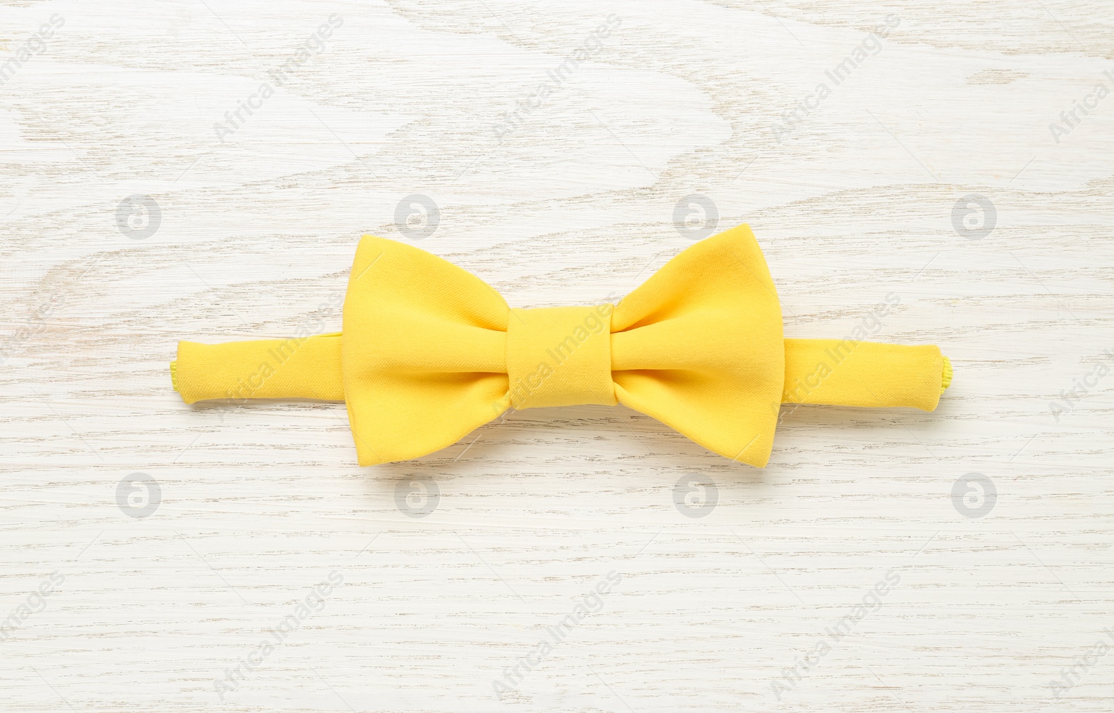 Photo of Stylish yellow bow tie on white wooden background, top view