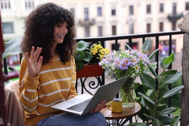 Photo of Beautiful young woman using laptop on balcony with green houseplants