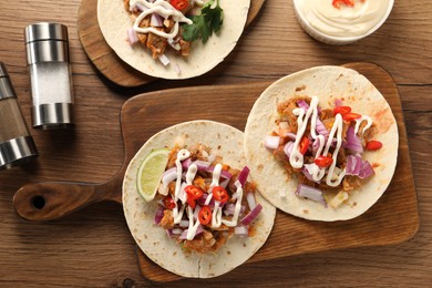 Delicious tacos with vegetables, meat and sauce on wooden table, flat lay