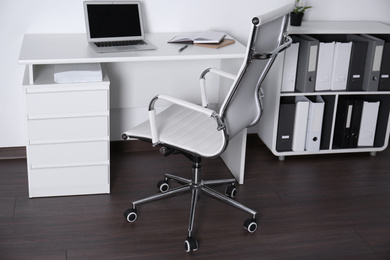 Photo of Comfortable rolling chair near table with laptop in modern office