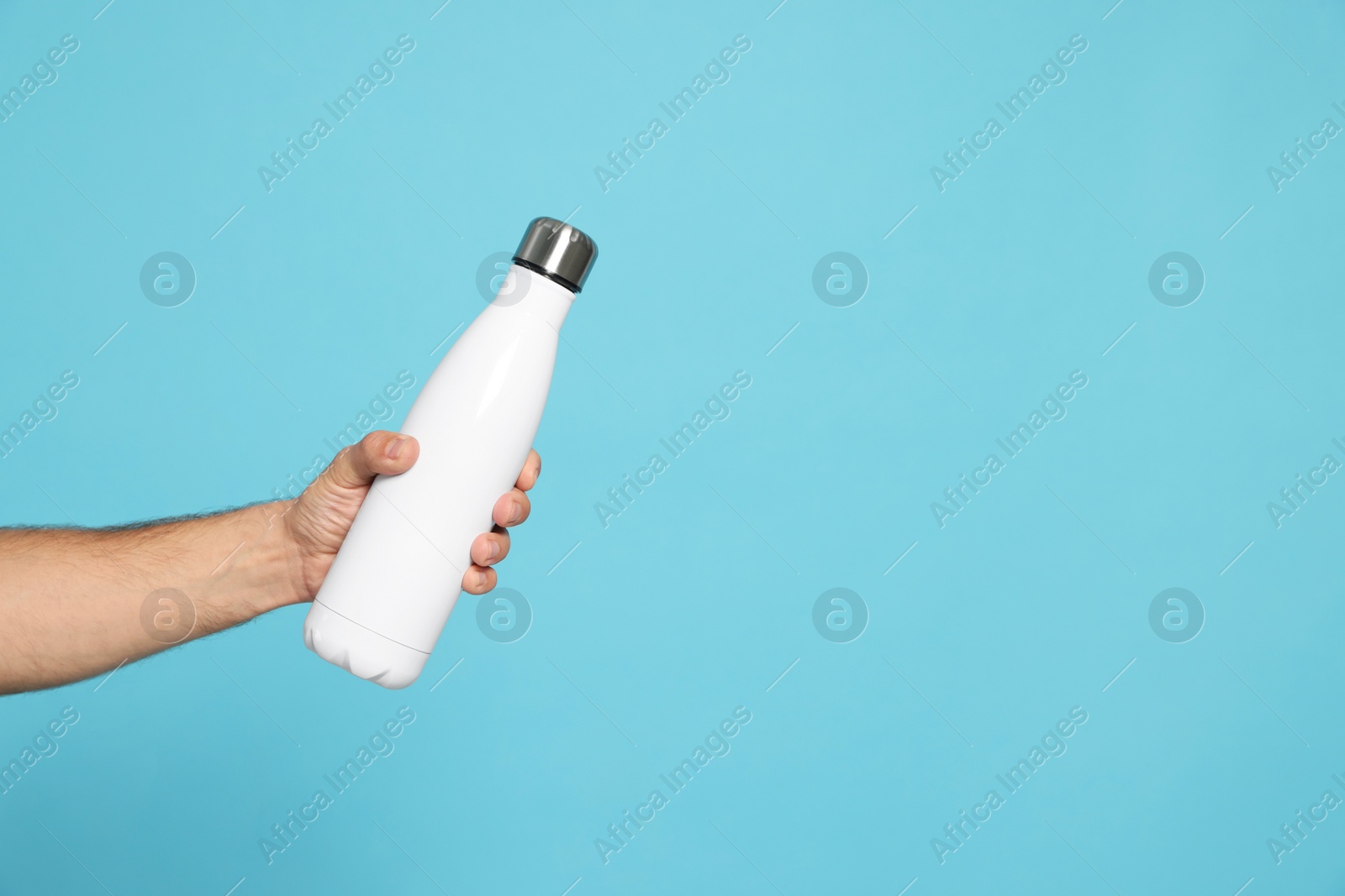 Photo of Man holding thermo bottle on light blue background, closeup. Space for text