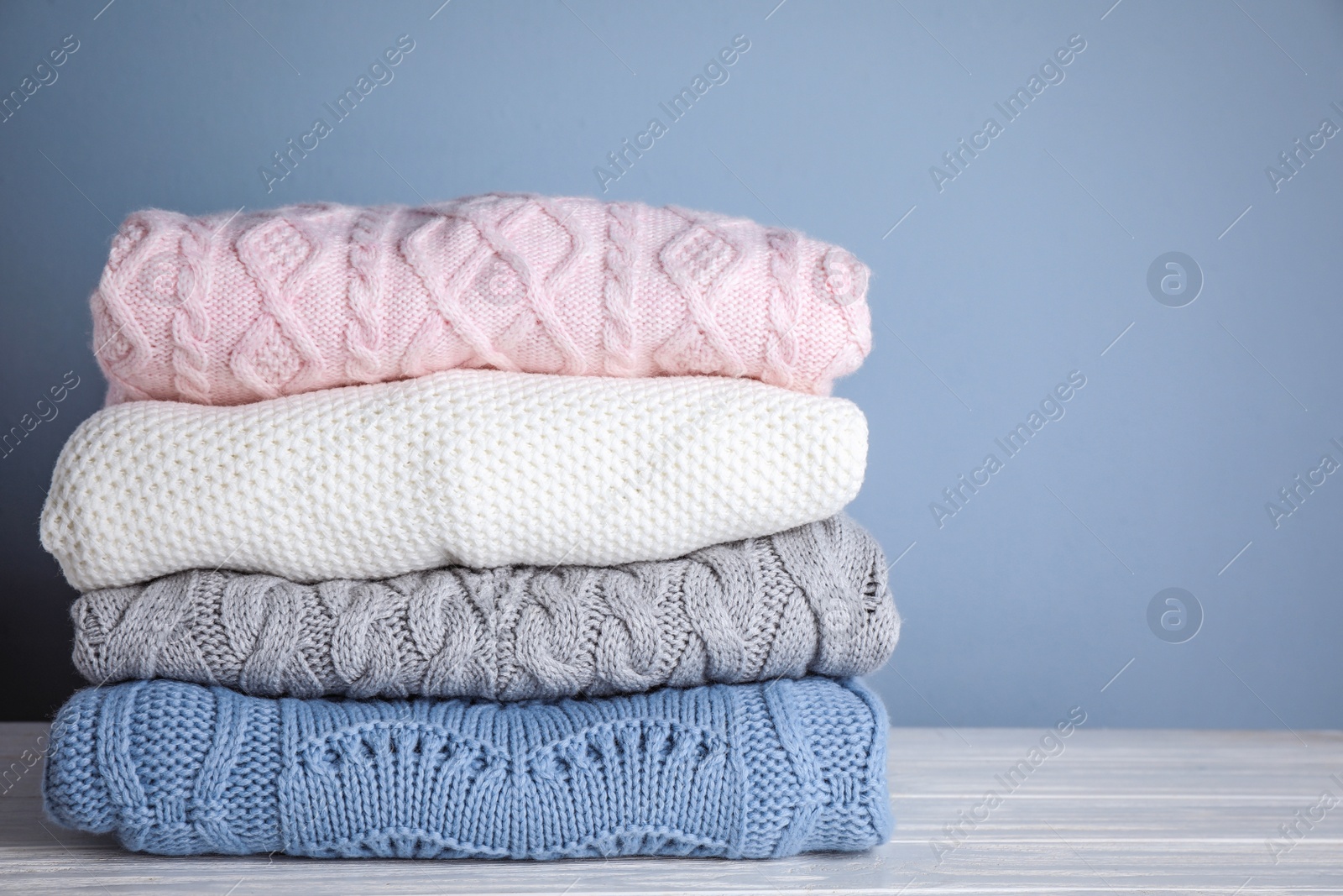 Photo of Stack of folded knitted sweaters on white wooden table against grey background. Space for text