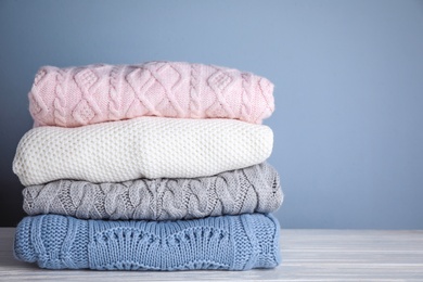 Photo of Stack of folded knitted sweaters on white wooden table against grey background. Space for text