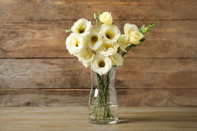 Photo of Beautiful white Eustoma flowers in vase on table against wooden background