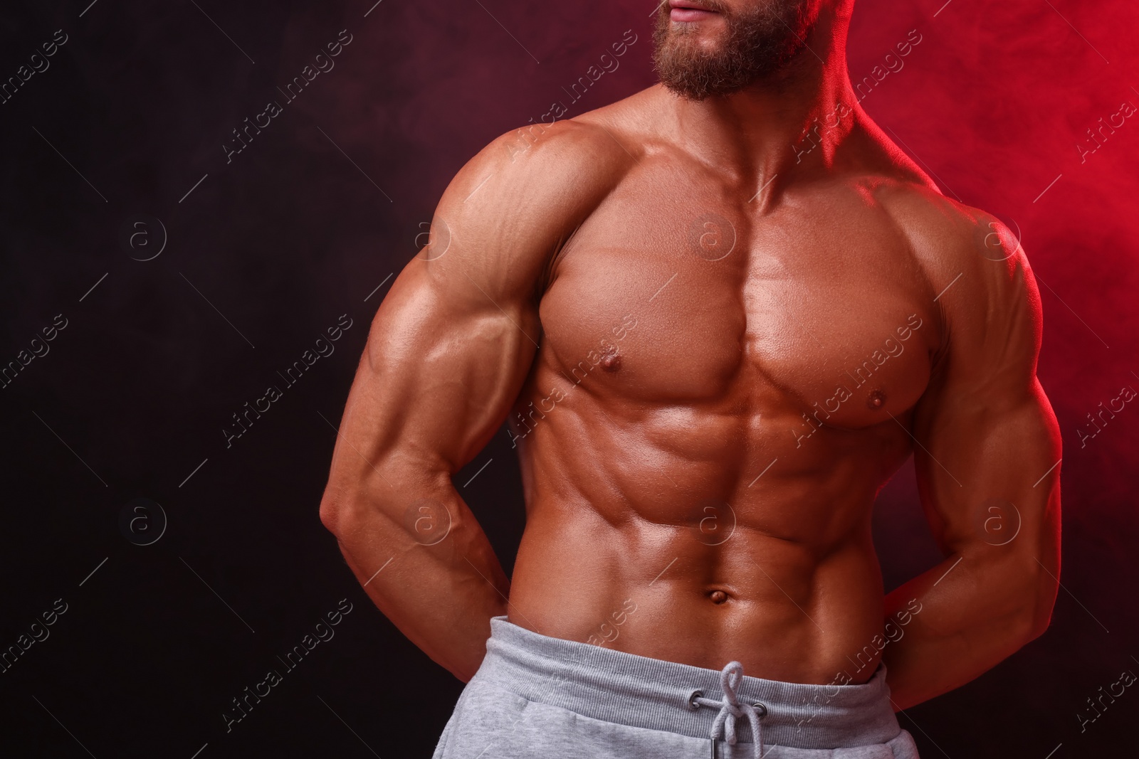 Photo of Young bodybuilder with muscular body in smoke on color background, closeup