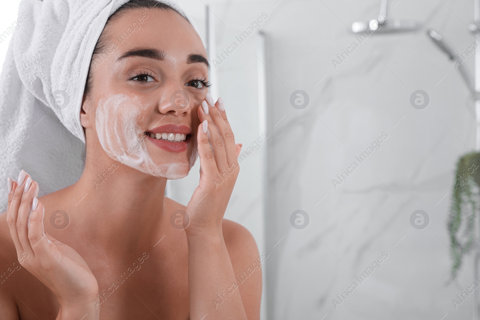 Photo of Beautiful young woman applying cleansing foam onto face in bathroom, space for text. Skin care cosmetic