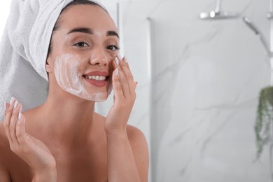 Beautiful young woman applying cleansing foam onto face in bathroom, space for text. Skin care cosmetic