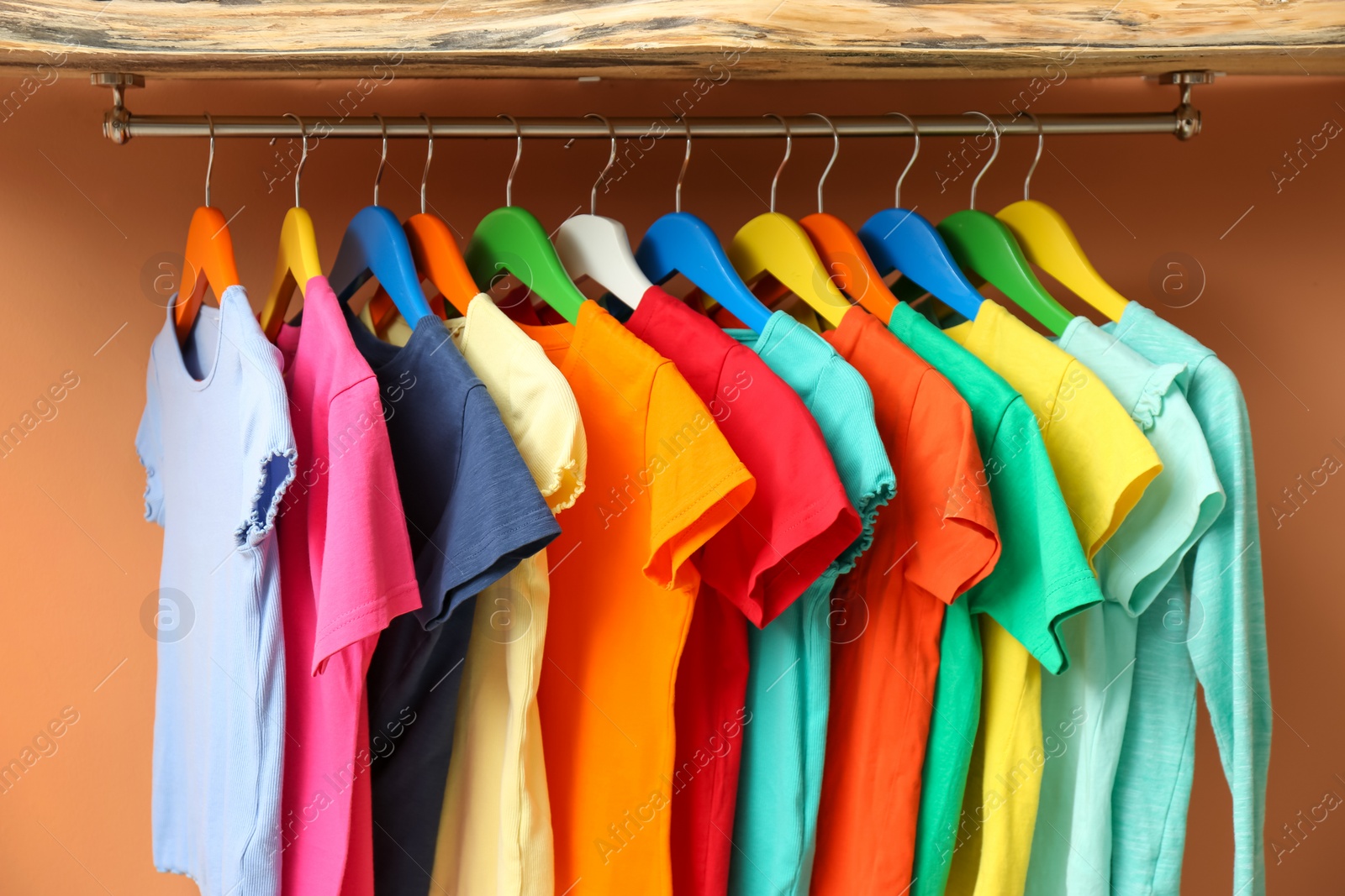 Photo of Rack with different child's clothes near coral wall, closeup