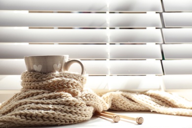 Photo of Cup of hot winter drink with scarf on windowsill indoors. Space for text