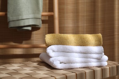 Photo of Stacked soft towels on wicker bench indoors, space for text