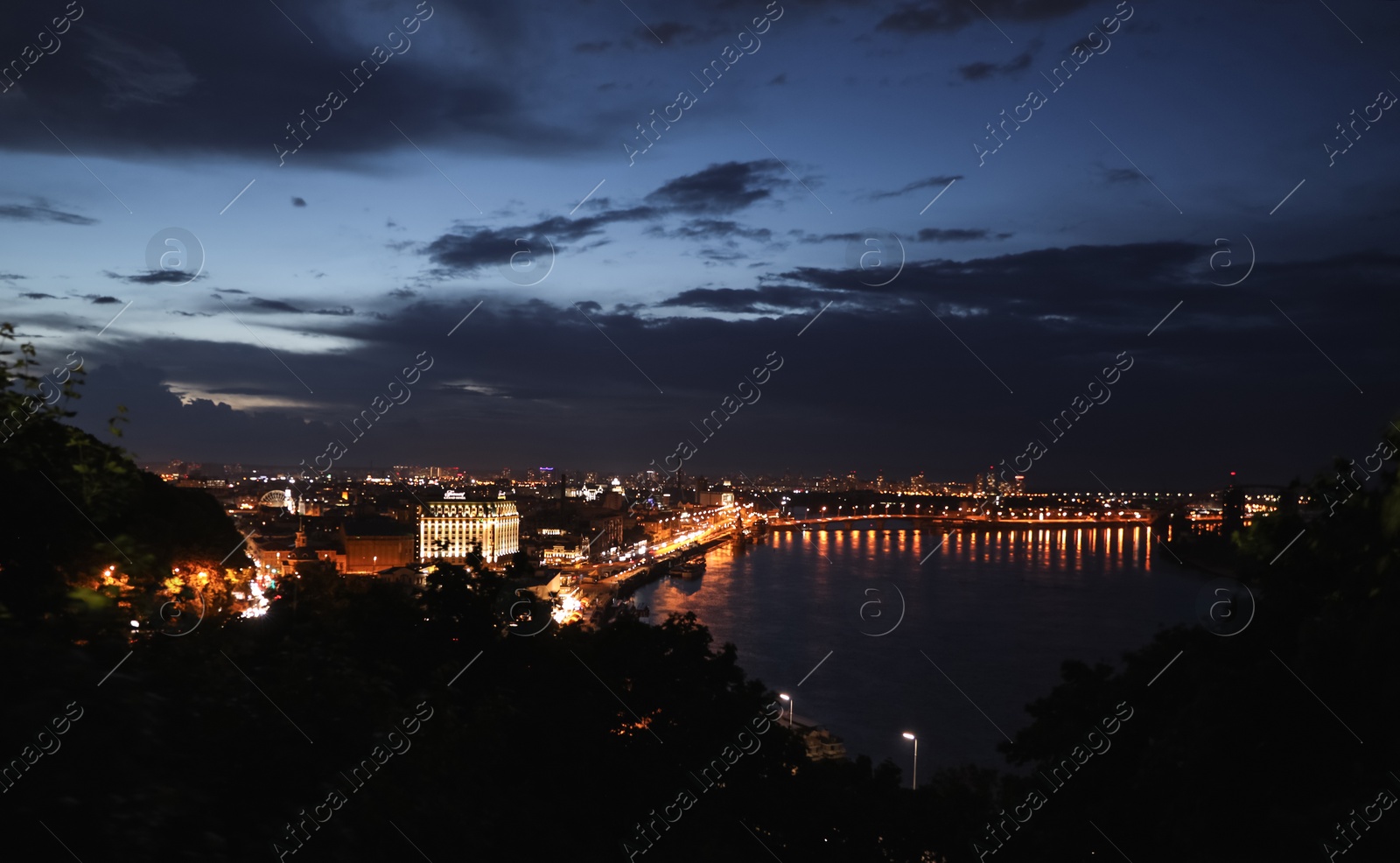 Photo of KYIV, UKRAINE - MAY 21, 2019: Beautiful view of night cityscape with illuminated buildings near river and bridge