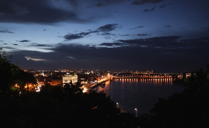 KYIV, UKRAINE - MAY 21, 2019: Beautiful view of night cityscape with illuminated buildings near river and bridge