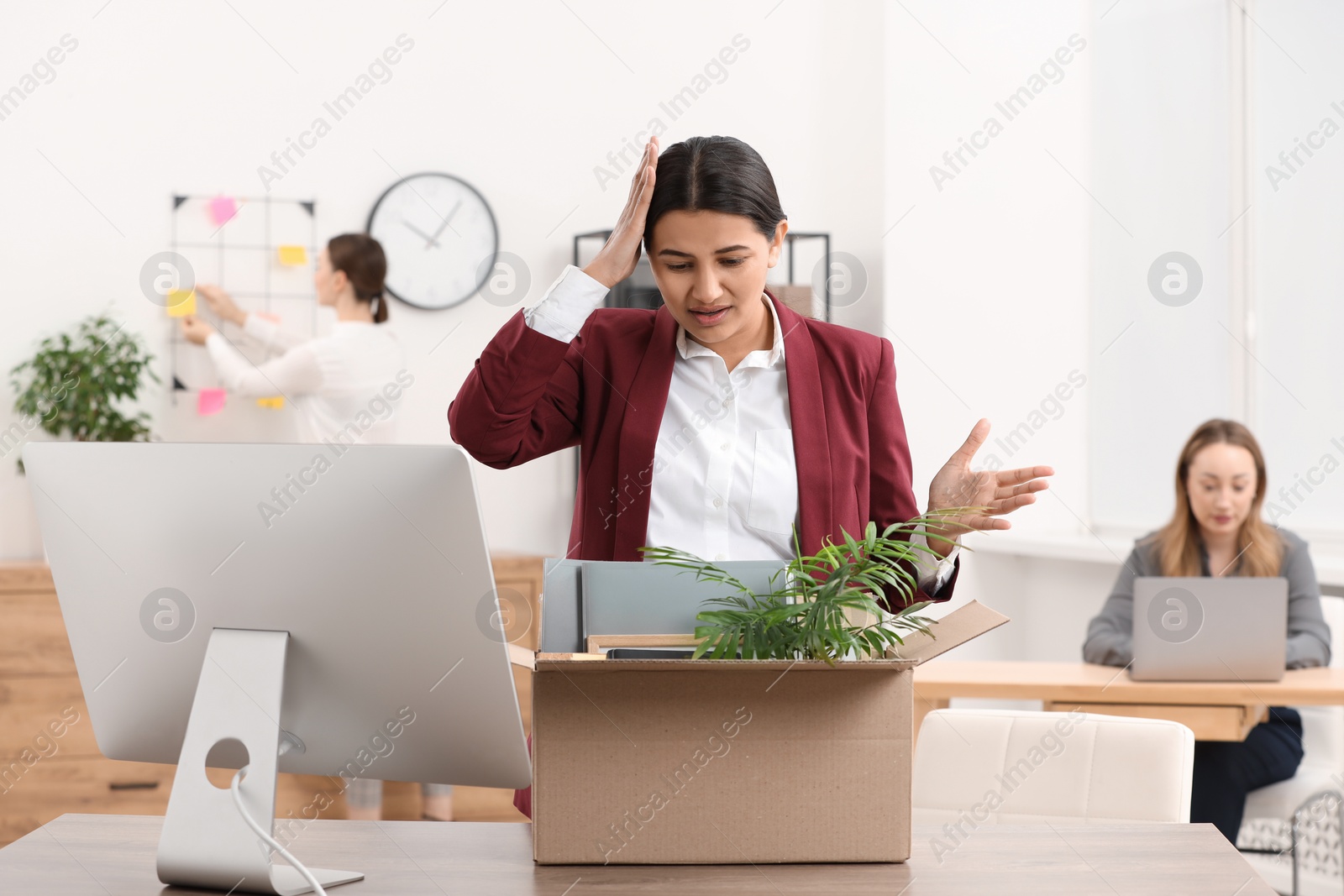 Photo of Unemployment problem. Worried woman with box of personal belongings at table in office